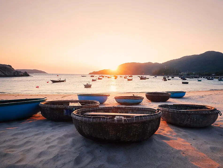 Round basket boats resting on the sand at sunset with soft light over the shoreline.