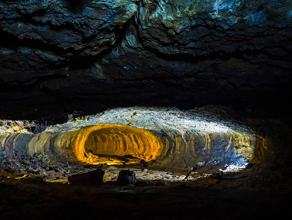 Long volcanic tunnel with layered volcanic textures glowing under artificial cave lighting.