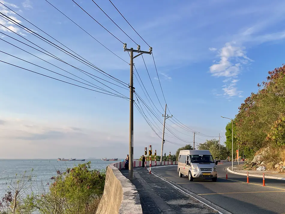 Tourist van driving along a scenic coastal road with ocean views and cliffs alongside.