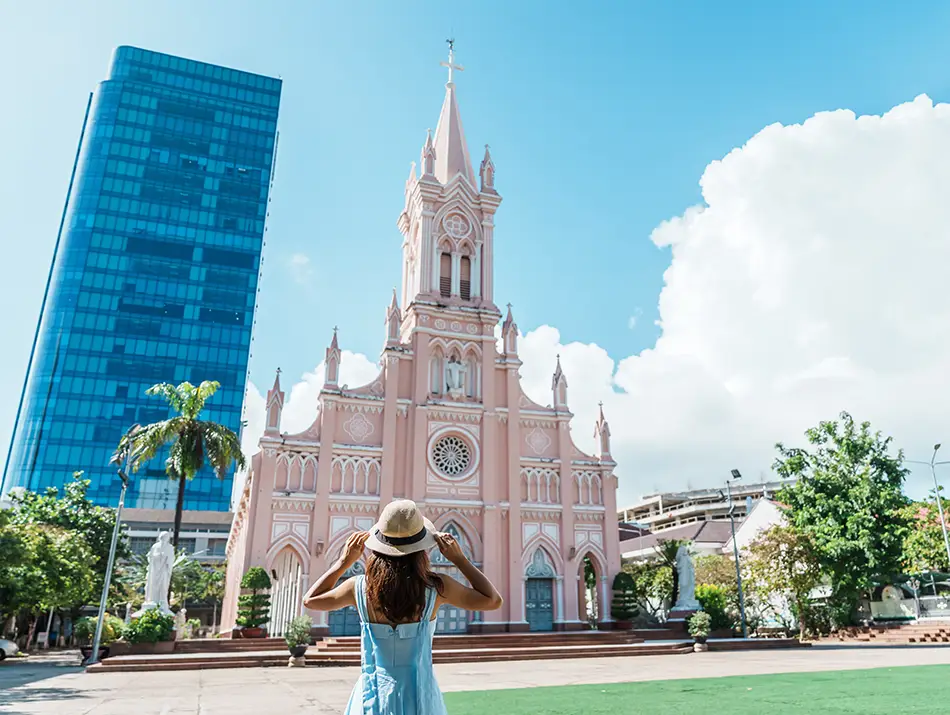 The pink Gothic-style Da Nang Cathedral framed by blue skies and palm trees.