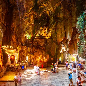 Visitors walking inside a large illuminated cave chamber with statues and glowing altars.