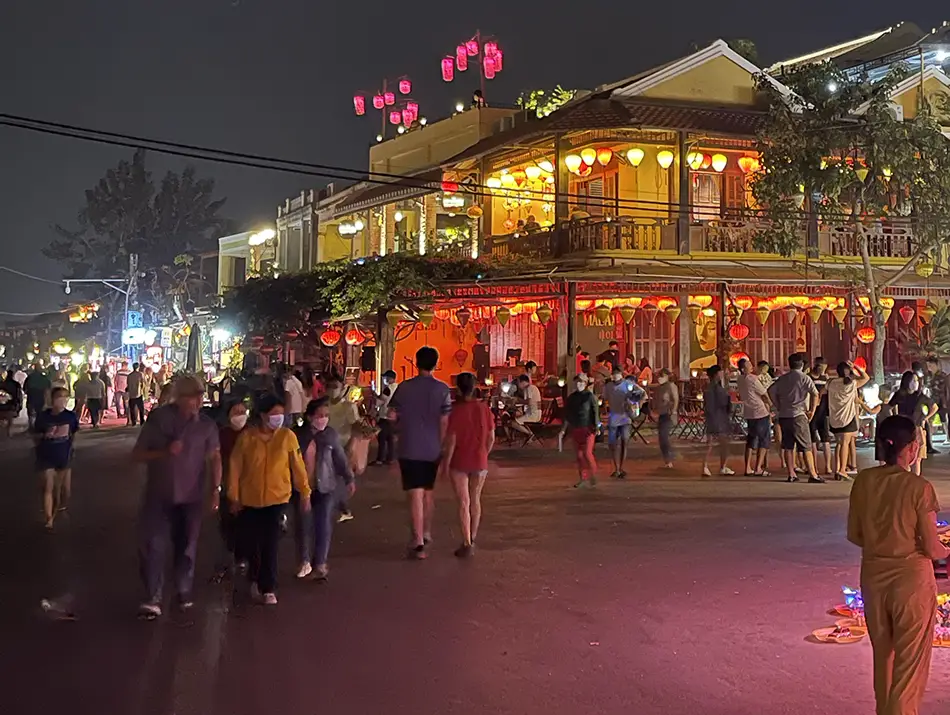 Crowds move through glowing streets filled with shops, cafés, and warm lights.