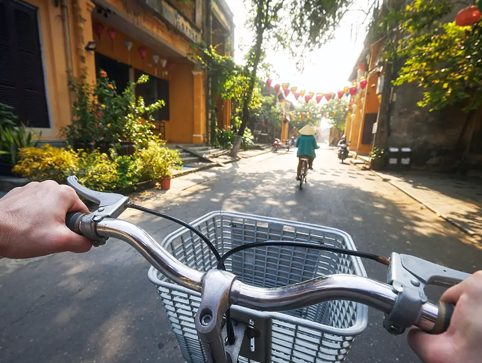 Cyclist riding through lantern-decorated old town streets, showing getting around Hoi An by bicycle.