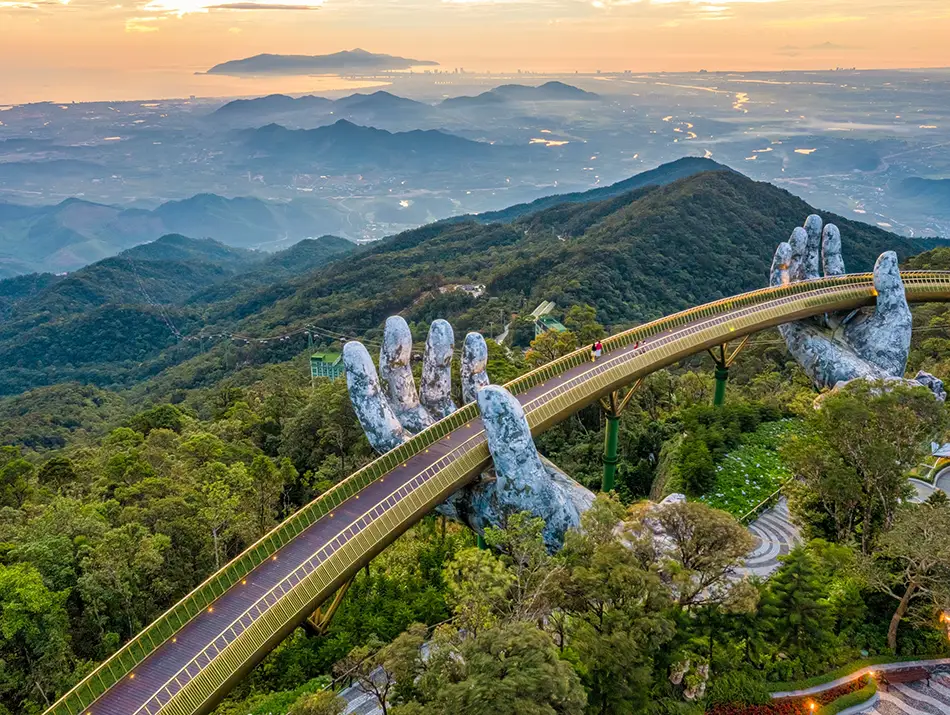 The Golden Bridge curving above forested mountains during sunrise.