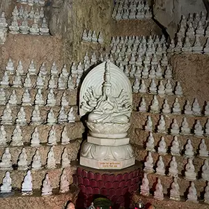 Rows of small carved Buddha figures displayed along a stone wall beside a larger statue.