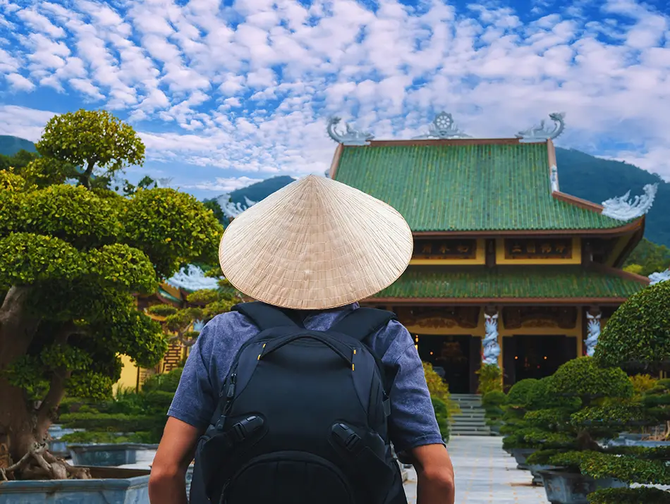 Backpacker facing Linh Ung Pagoda gardens and temple roofs on Son Tra Peninsula.