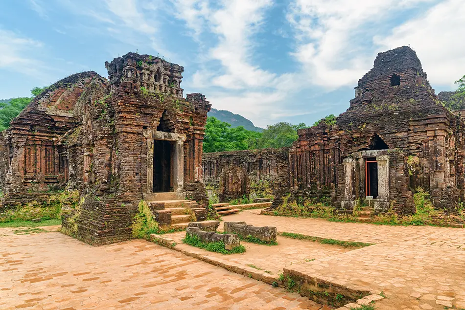 A cluster of ancient Cham temple ruins surrounded by hills and open space.
