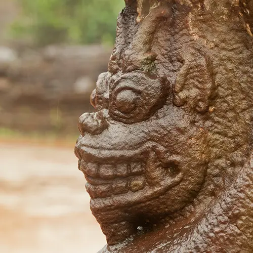 A close-up of a weathered stone guardian carving with intricate facial details.