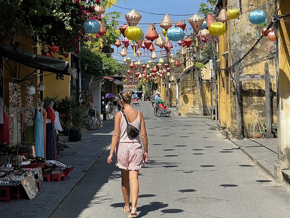 A quiet daytime walk passes yellow houses and hanging lanterns overhead.