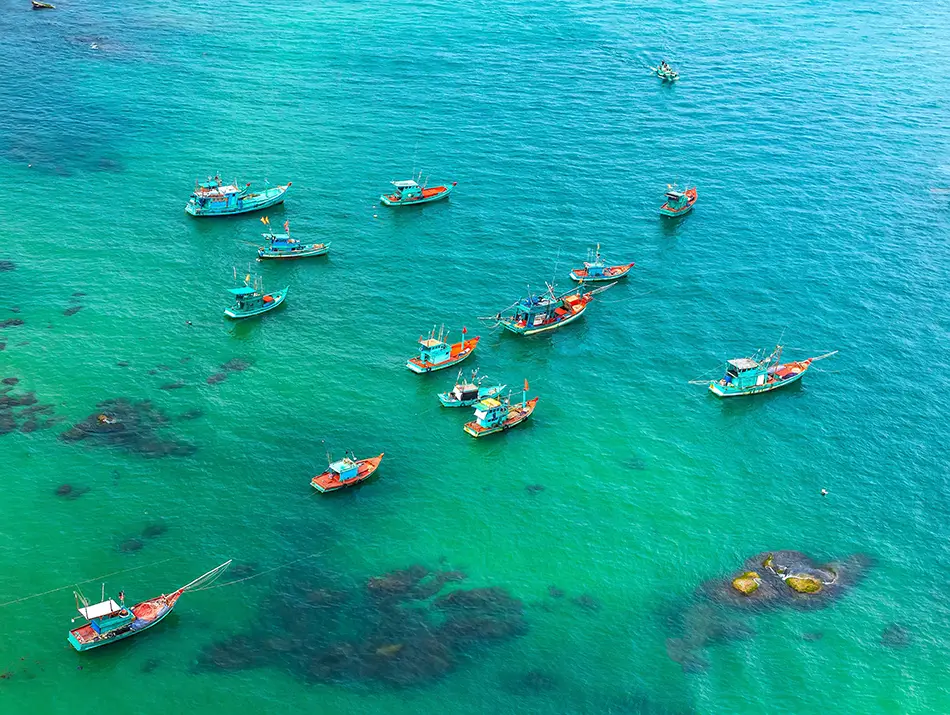 Numerous small boats floating on vibrant turquoise waters surrounded by coral reefs, showcasing one of the best things to do on Phu Quoc Island.