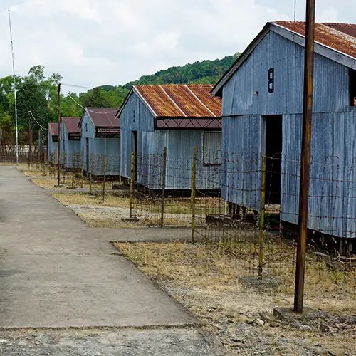 Weathered wooden buildings along a concrete pathway in the historic Coconut Tree Prison.