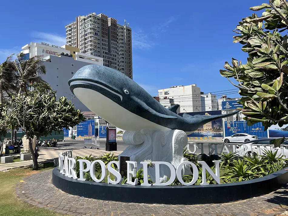 Whale statue from the Poseidon hotel area surrounded by greenery and city buildings