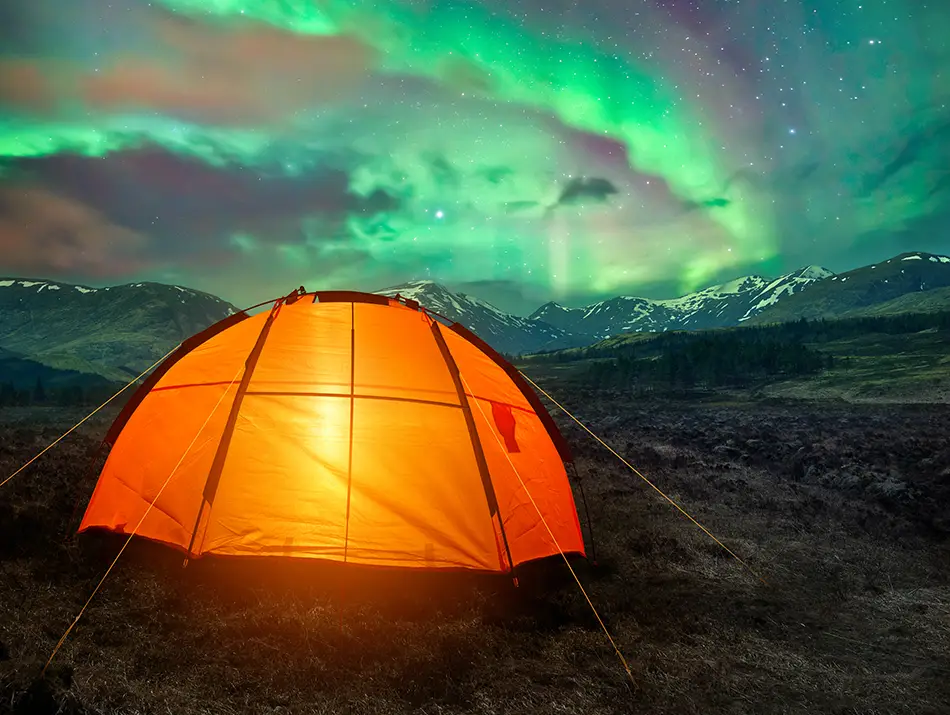 Glowing orange tent beneath a swirling green aurora in deep winter darkness.