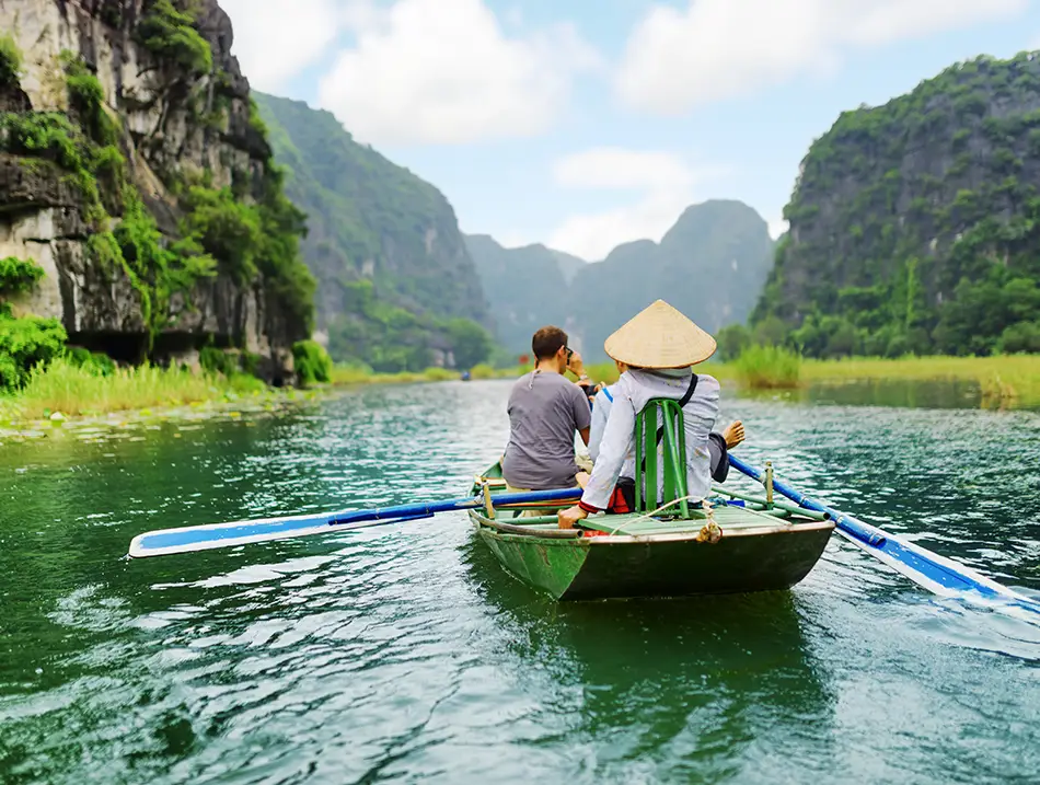 Small rowboat with a conical-hat rower and guests, getting around Ninh Binh Area on the river.