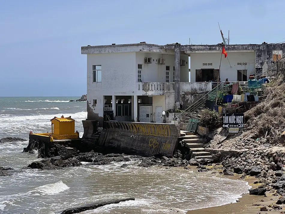 Weathered concrete structure perched on rocks beside crashing waves at high tide.