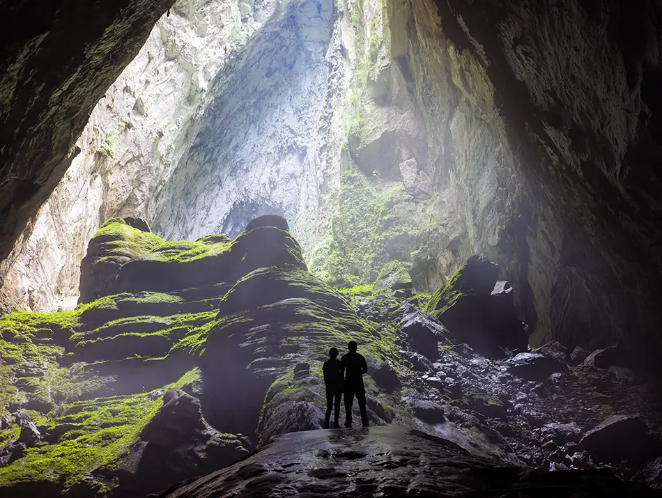 Sunlight pours into massive cave collapse revealing forest, moss, and towering rock walls.