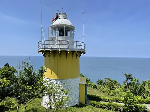 A yellow coastal lighthouse surrounded by greenery above the sea.