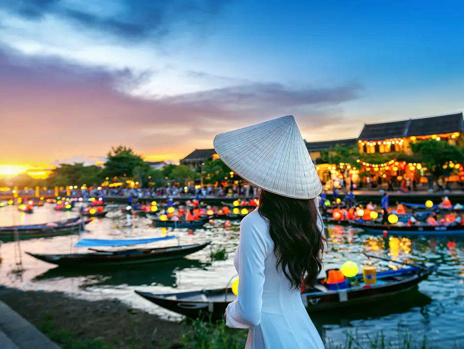 A traveler in traditional Ao Dai dress standing next to the river in Hoi An