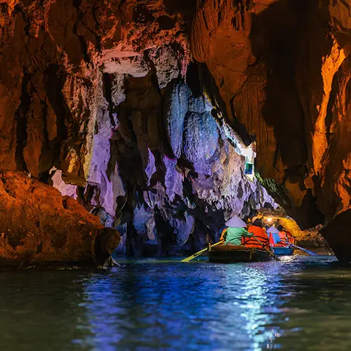 Rowing boat entering illuminated limestone cave along an underground river.