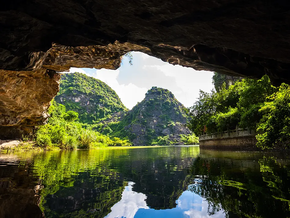 Natural limestone arch framing a calm water passage and lush greenery in Trang An.