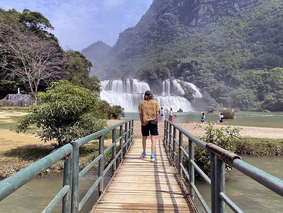 Traveler casually walking toward Ban Gioc Waterfall.