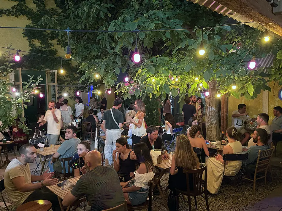 Crowded open-air bar scene captures Yerevan nightlife with friends chatting under string lights.