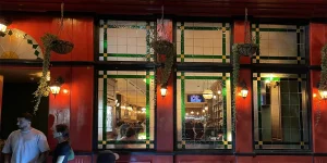 Pub exterior shows illuminated windows, street-facing tables, and a welcoming evening glow.