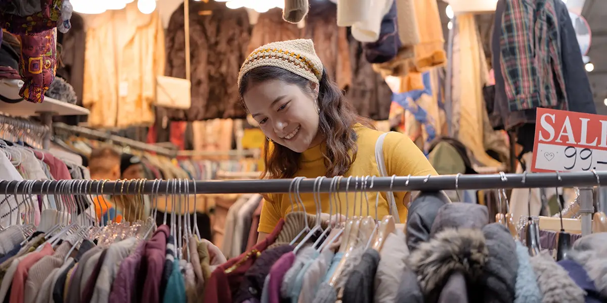 Woman browsing a vintage clothing rack in a market, new shopping destinations hero.