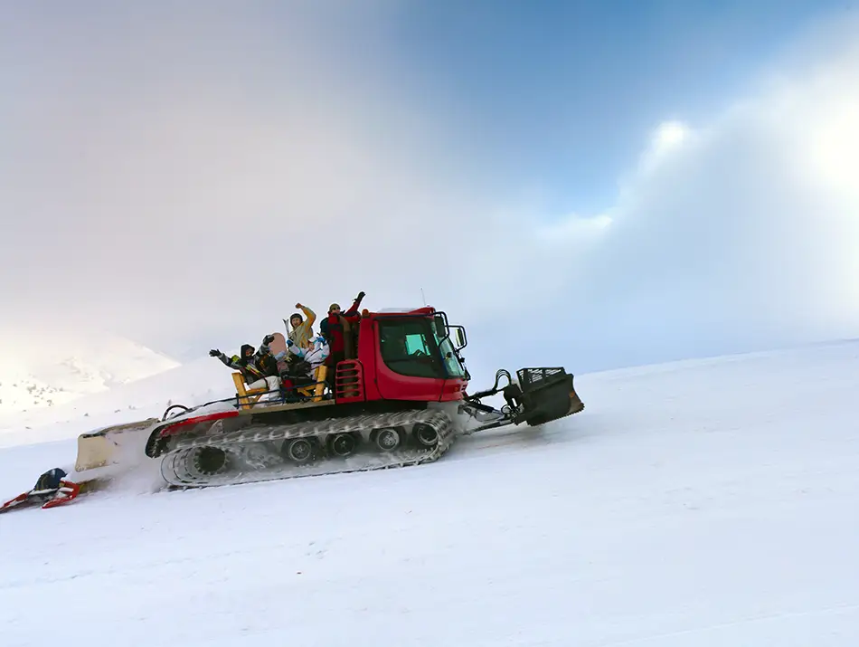 Snow groomer climbs a fresh powder slope under a breaking winter sky.