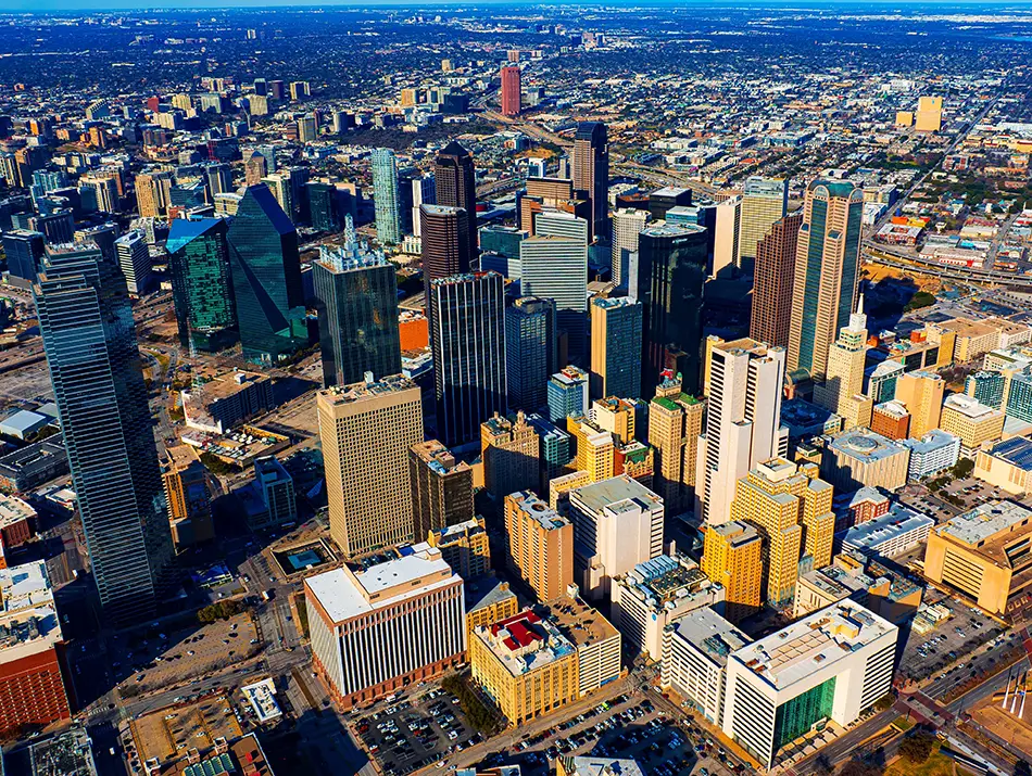 Aerial view of a downtown skyline with glass towers, freeways, and afternoon shadows.