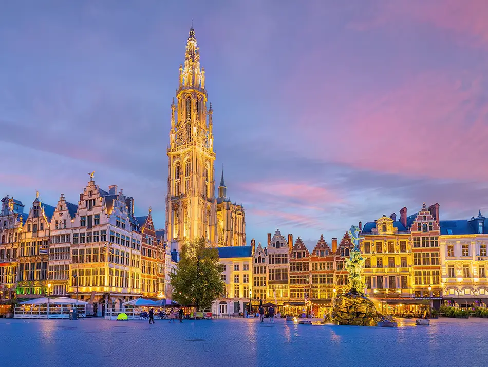 Historic riverside skyline at dusk with a tall Gothic cathedral spire reflected on water.