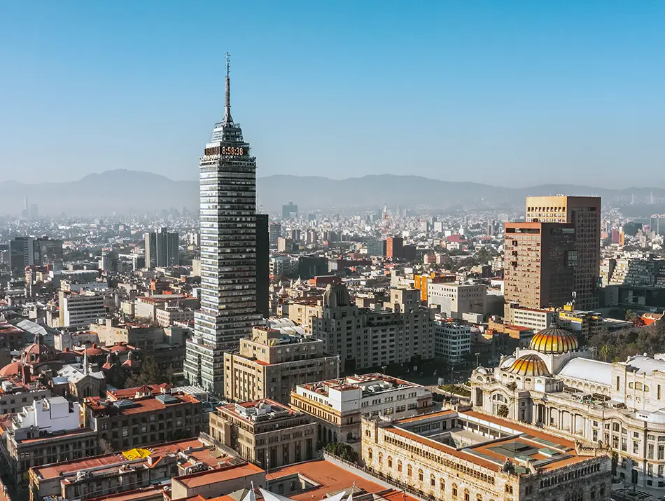City skyline with a tall art-deco tower rising above dense rooftops under clear skies.