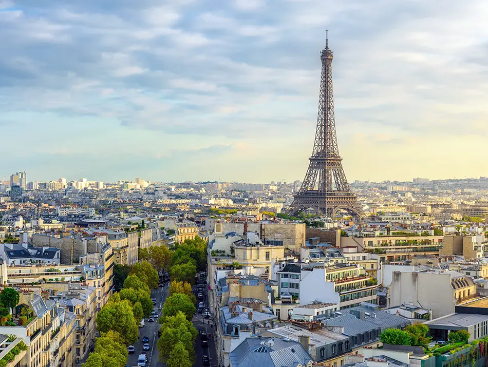 Wide boulevard leading to an iron tower above rooftops, photographed in soft morning light.