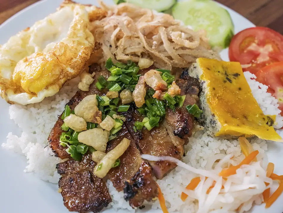 Com tam plate with grilled pork, fried egg, fresh cucumber, and pickles.