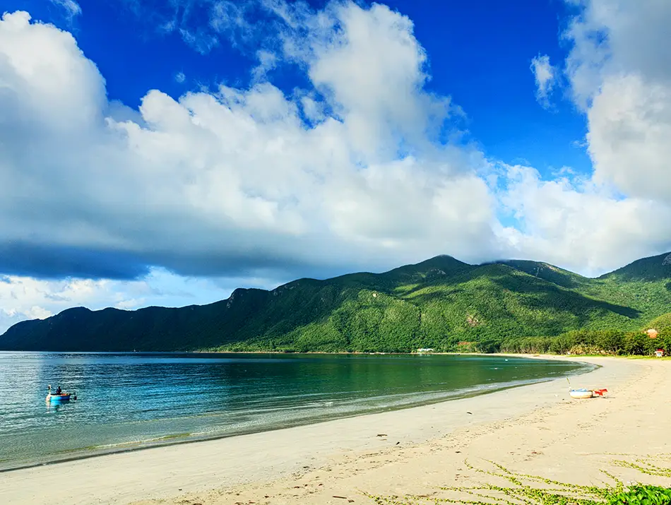Wide sandy shoreline curves along clear water with forested hills in the distance.