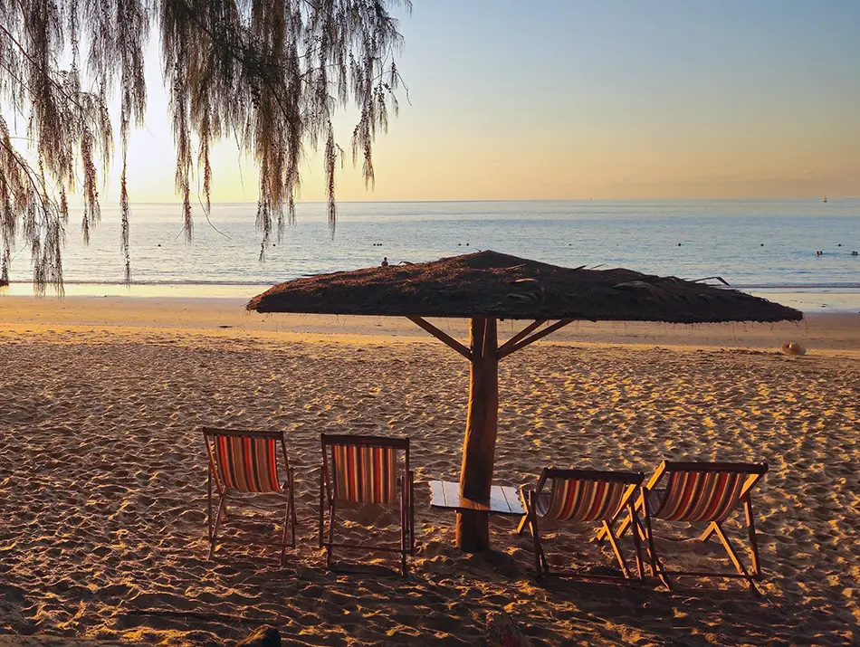 Empty sandy beach in Con Dao at sunset with striped deck chairs under a thatched umbrella, calm sea, and warm evening light, amongst the best places to visit in Vietnam if you dislike the crowds.