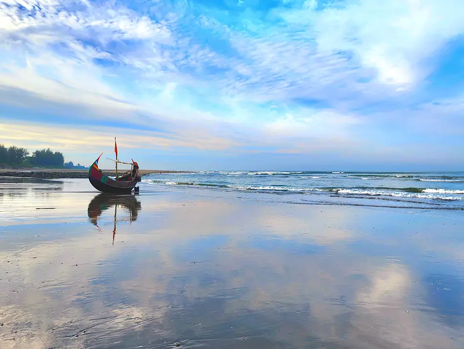 Traditional fishing boat on Cox’s Bazar beach at low tide, surf horizon behind.