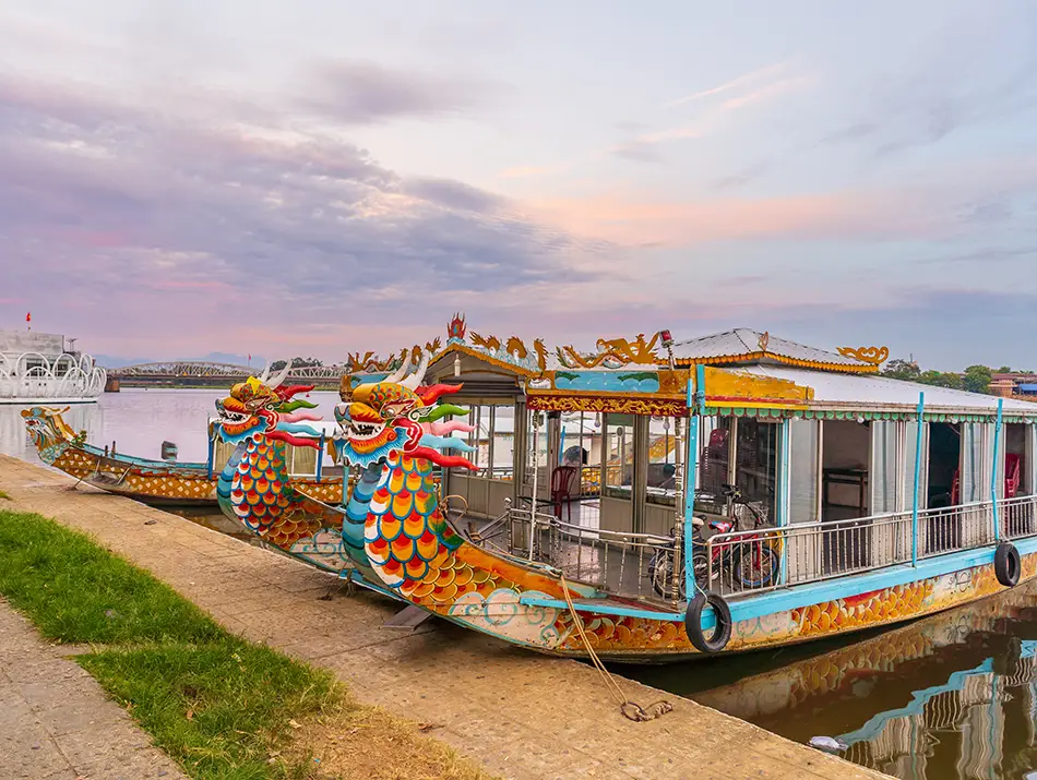 Long wooden dragon boat with covered seating docked on calm river