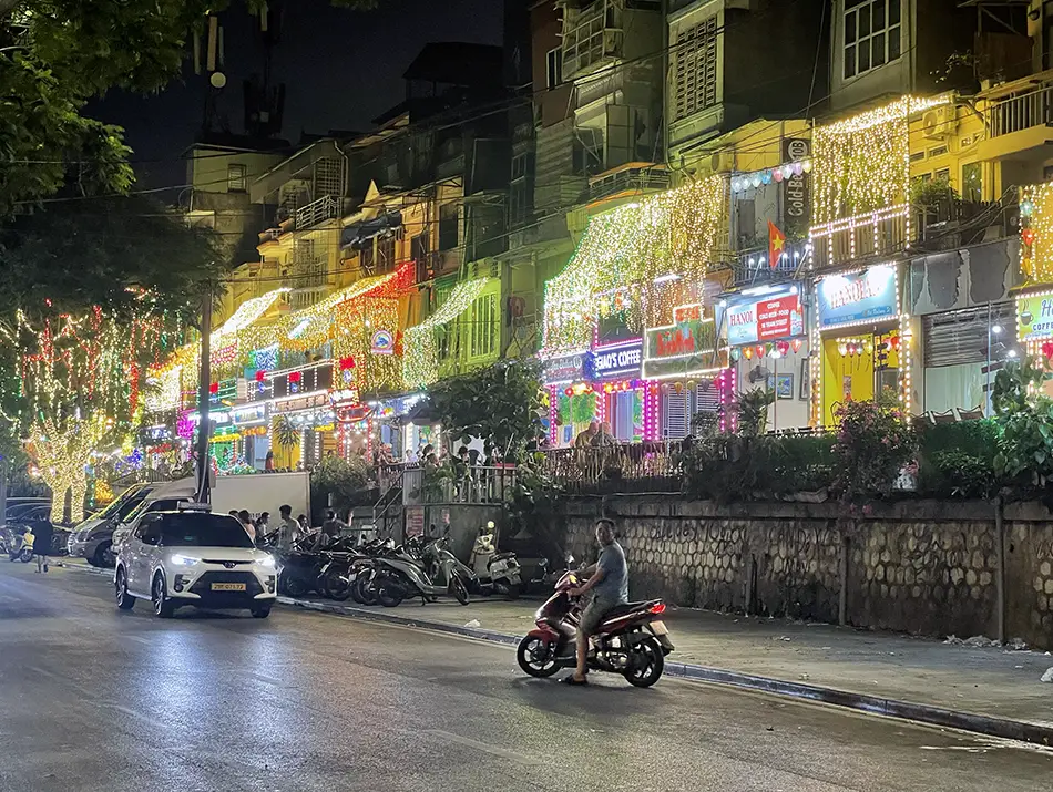 Evening street scene with glowing shop signs and motorbikes, showing everyday activities in hanoi.