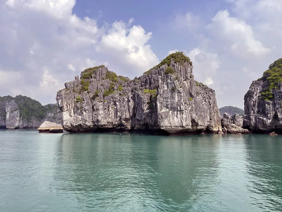 Limestone karsts rise sharply from calm water in Ha Long Bay, a classic example of things to see in Vietnam.