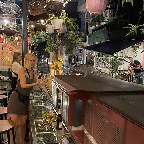 Narrow residential alley with lit homes and railway tracks stretching into the distance at night.