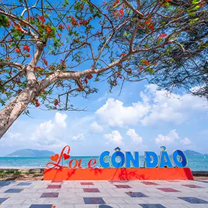Colorful beach sign reading ‘Love Con Dao’ set against blue sky, trees, and distant ocean views.