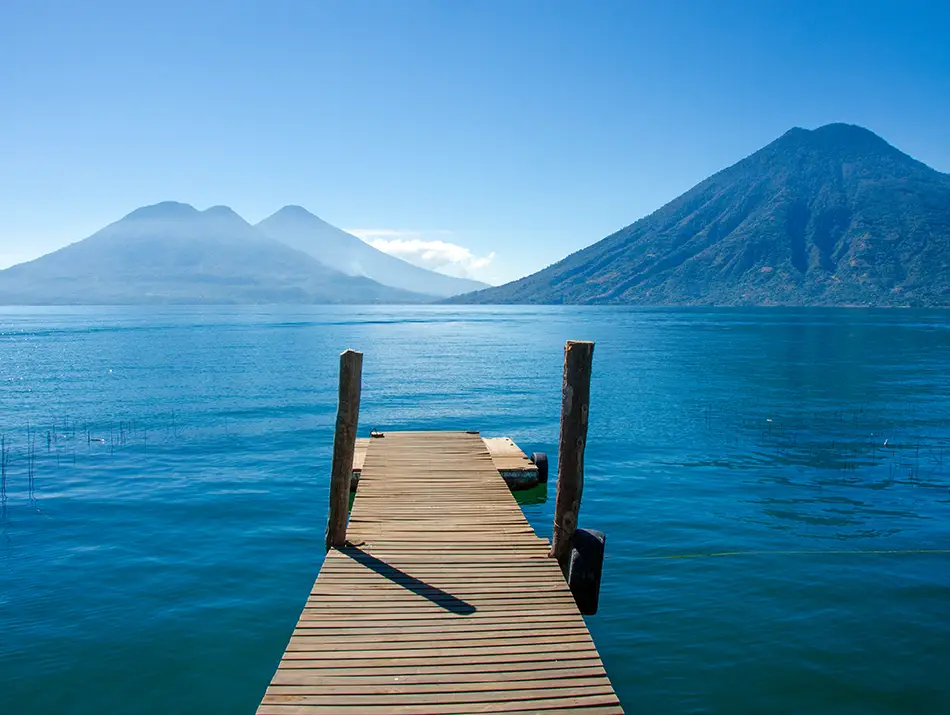 Wooden pier extending into Lake Atitlan with volcanoes in the background.