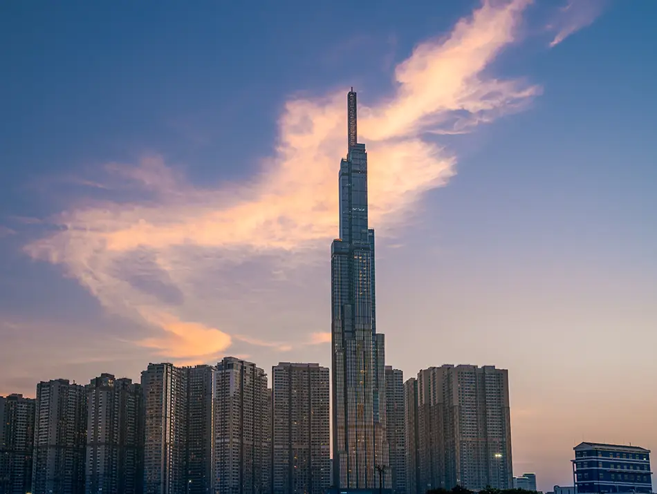 Tall skyscraper rises above the skyline during sunset with glowing clouds.