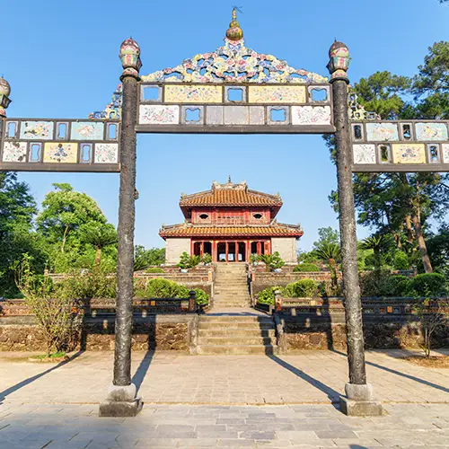 Ceremonial stone gate framing a straight walkway toward a yellow-roofed building.