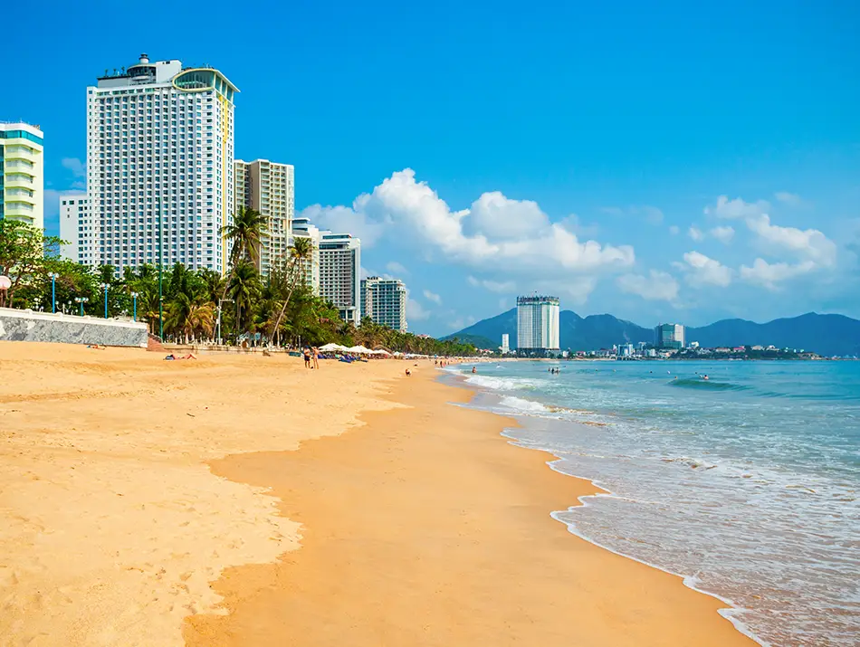 Wide golden sand curve with turquoise water and modern seaside high-rises under clear sky.