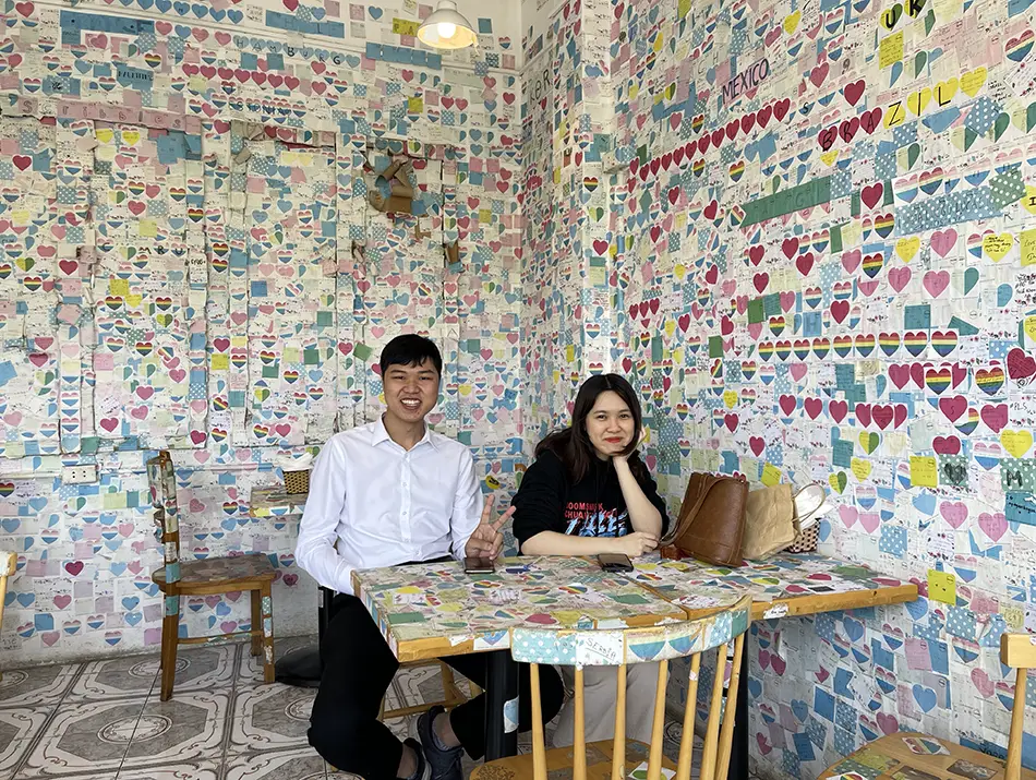 Two visitors seated at a small table surrounded by walls covered in handwritten notes
