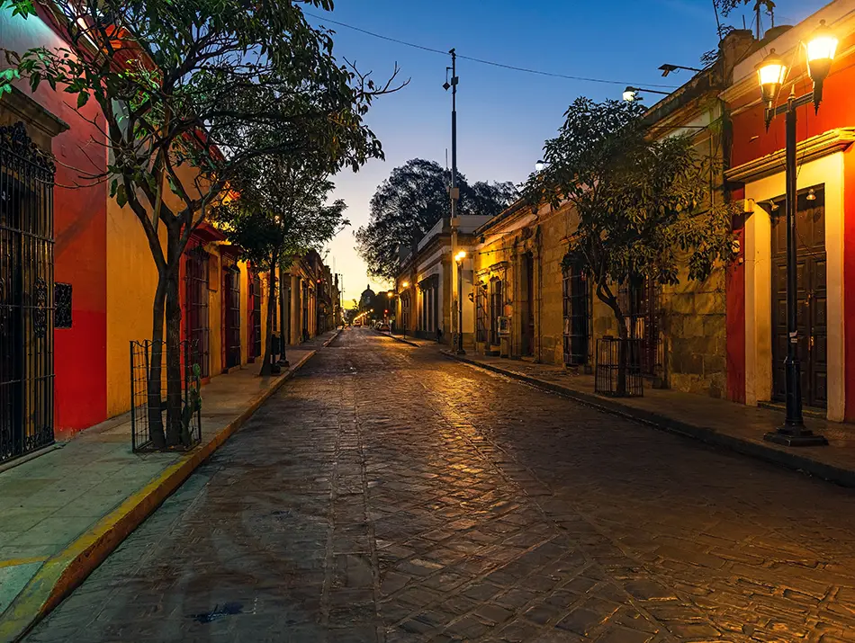 Colorful colonial street in Oaxaca City lit by warm evening lights.