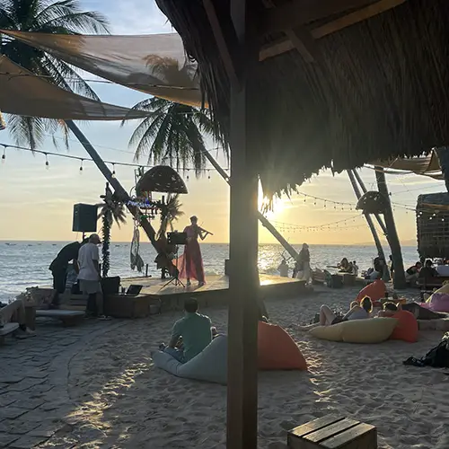 Palm-fringed beach seating with beanbags and a wooden hut at golden hour.