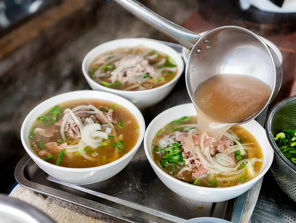 Fresh pho bowls are finished with hot broth and herbs at a local street stall.